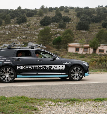 Team support car with cycling equipment driving on a scenic road.