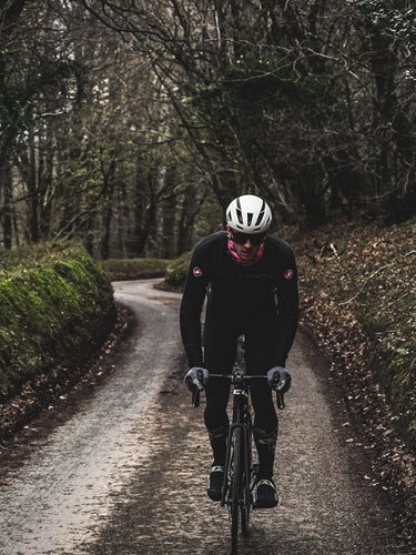 Cyclist riding on a winding country road surrounded by greenery and trees.